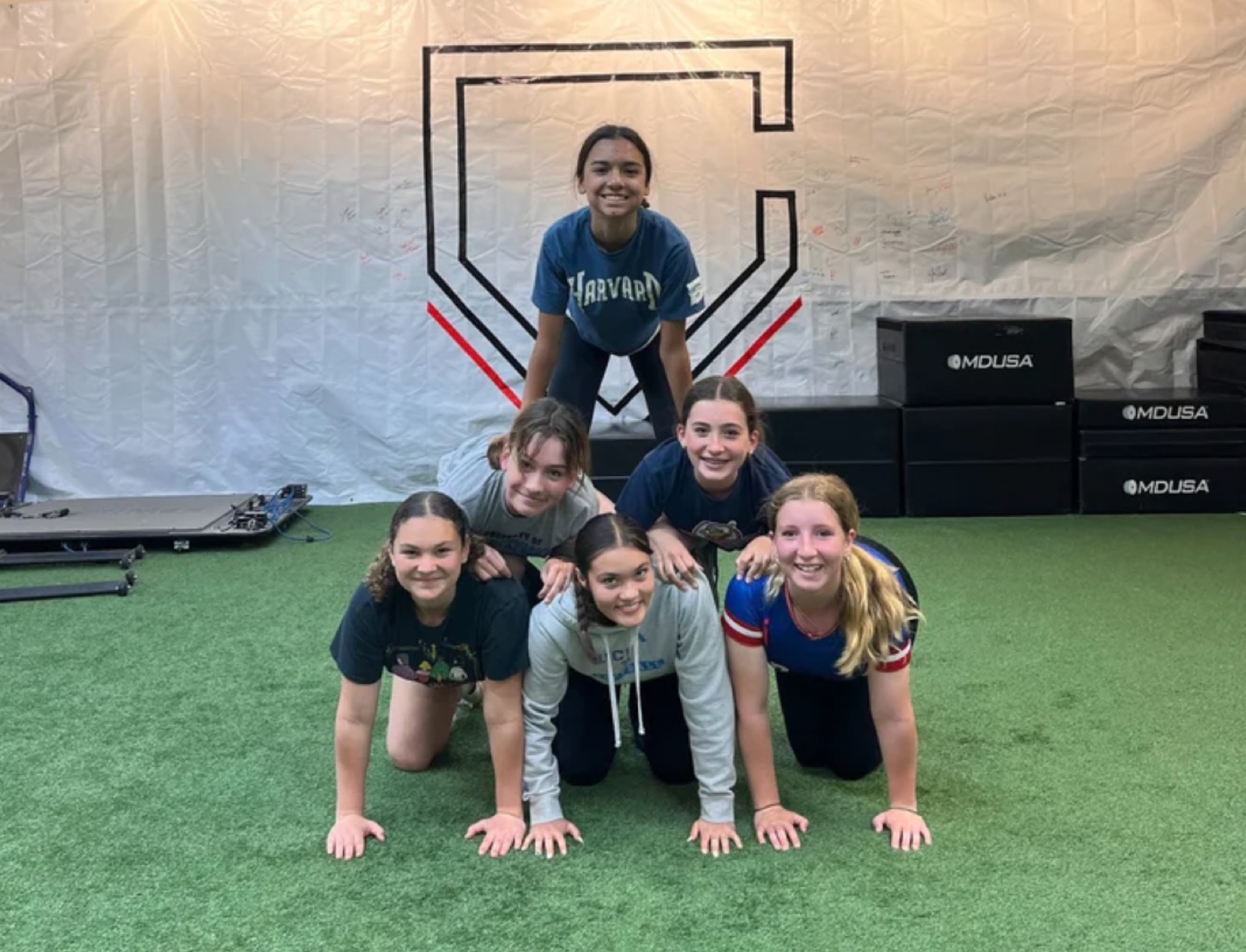 Six smiling softball players stacked in a human pyramid at The Clubhouse